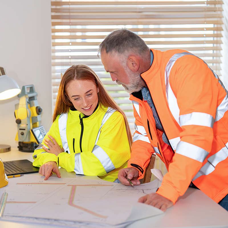 Apprentice and mentor looking over planning documents which lay on a table.