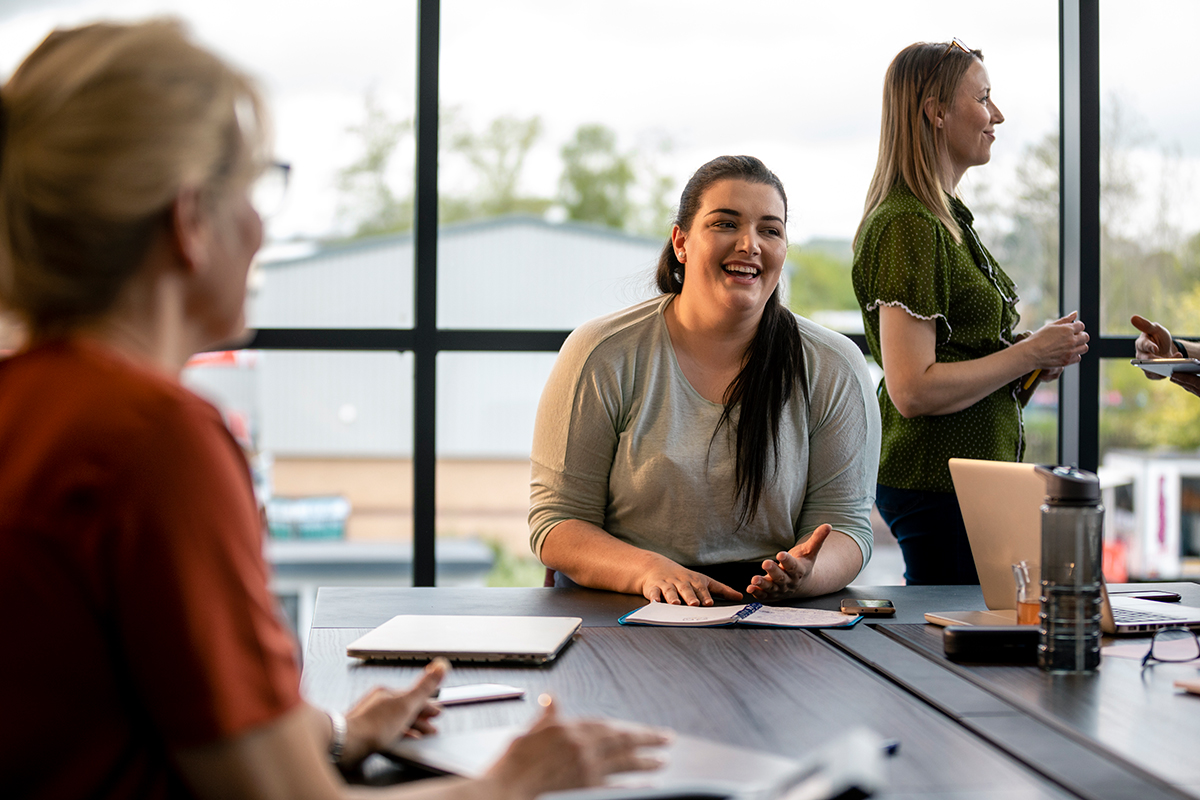 Young female Employee owner sat at a table meeting with other employee owners.