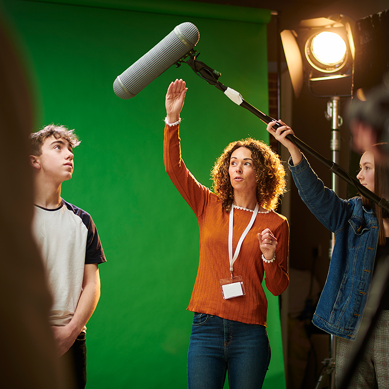 Three adults in a media studio putting sound equipment into place. 