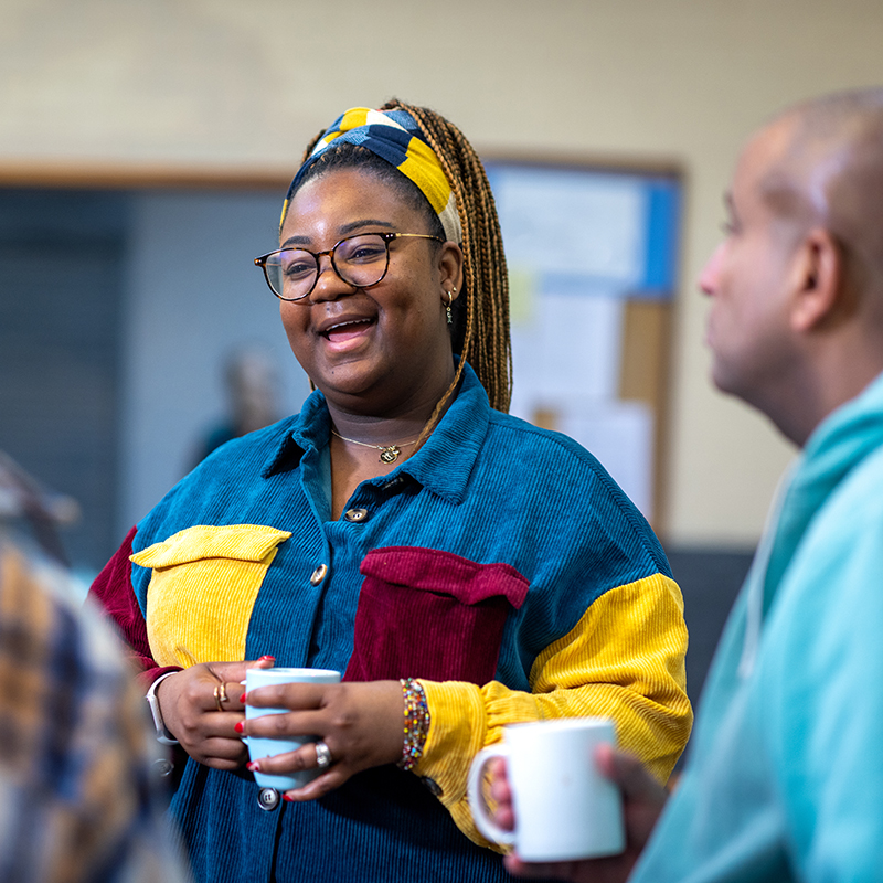 Smiling lady having a chat with other staff members over a cup of tea.