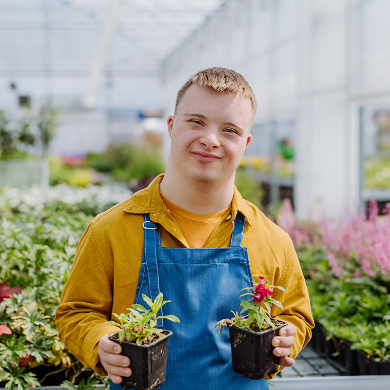 Smiling young adult with down syndrome at a community garden.