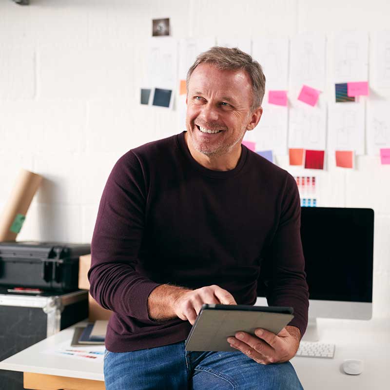 Man sitting on desk whilst holding a tablet.