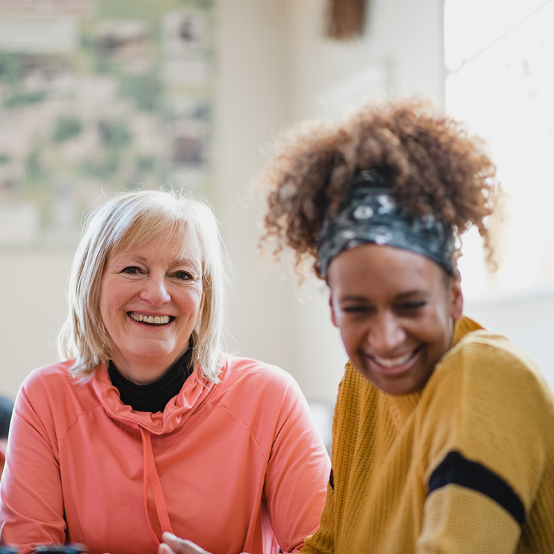 Two adults smiling together whilst sitting around a table at a community hub.