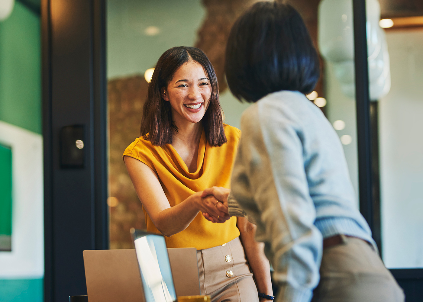 Businesswoman shaking hands with client and whilst smiling in meeting room.
