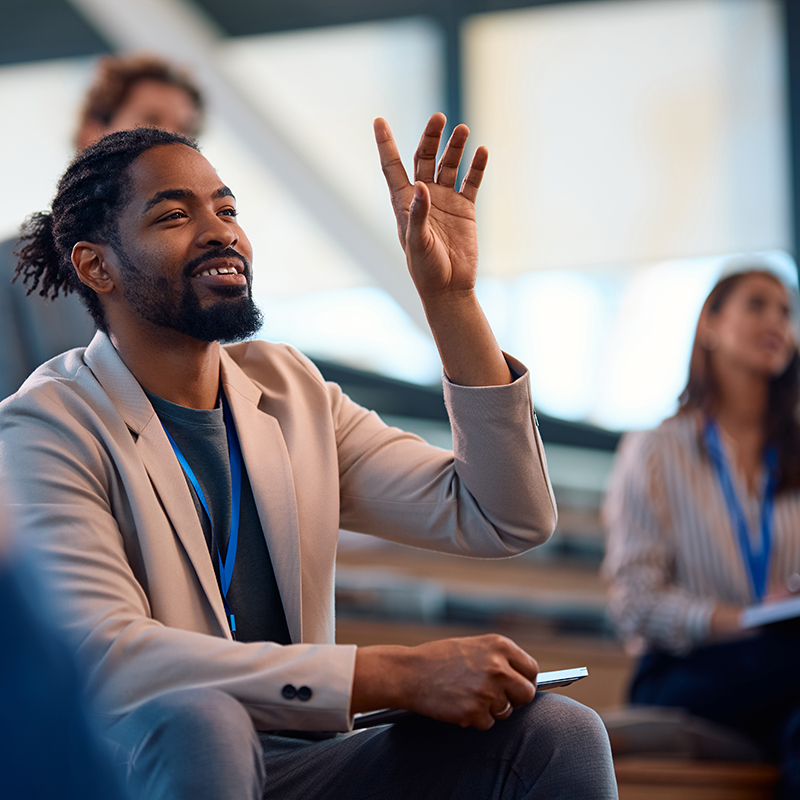 Businessman raising his arm to ask a question during a commercial training course in a classroom setting.