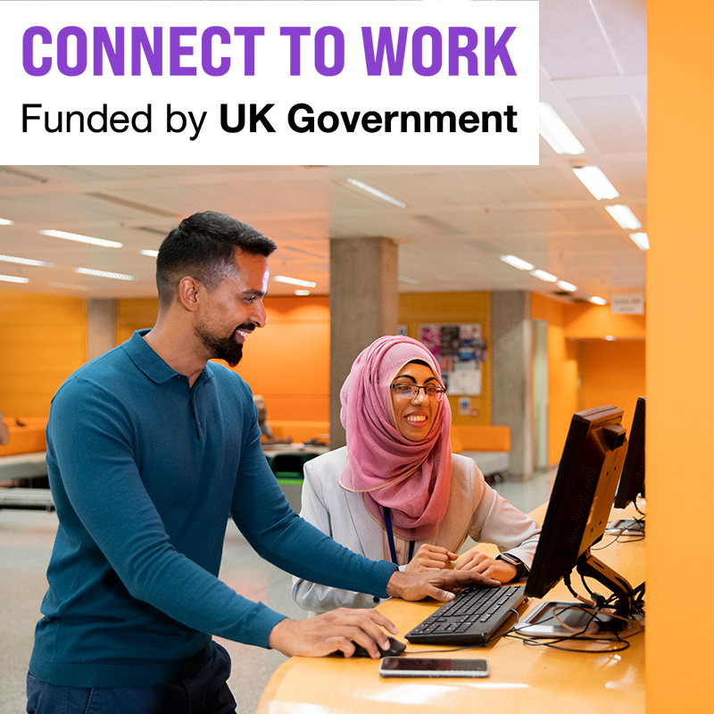Work coach and participant stand together whilst working on a computer