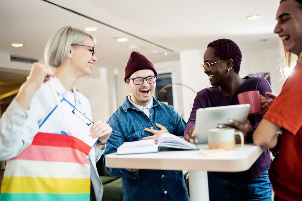 Four work colleagues share a joke together whilst standing over a desk.